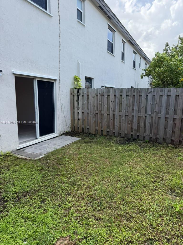 Exterior space featuring a grassy lawn, a vertical wood privacy fence, and a sliding glass door with a concrete patio landing