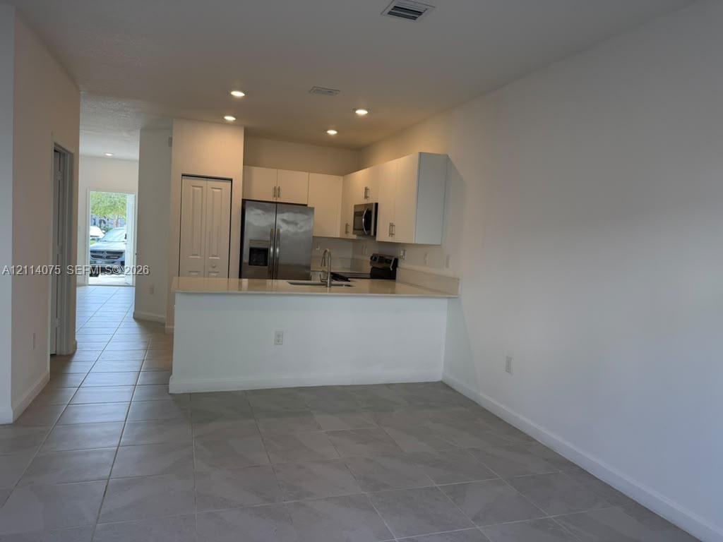 Kitchen featuring white cabinetry, solid-surface countertops, recessed lighting, tile flooring, and stainless steel appliances
