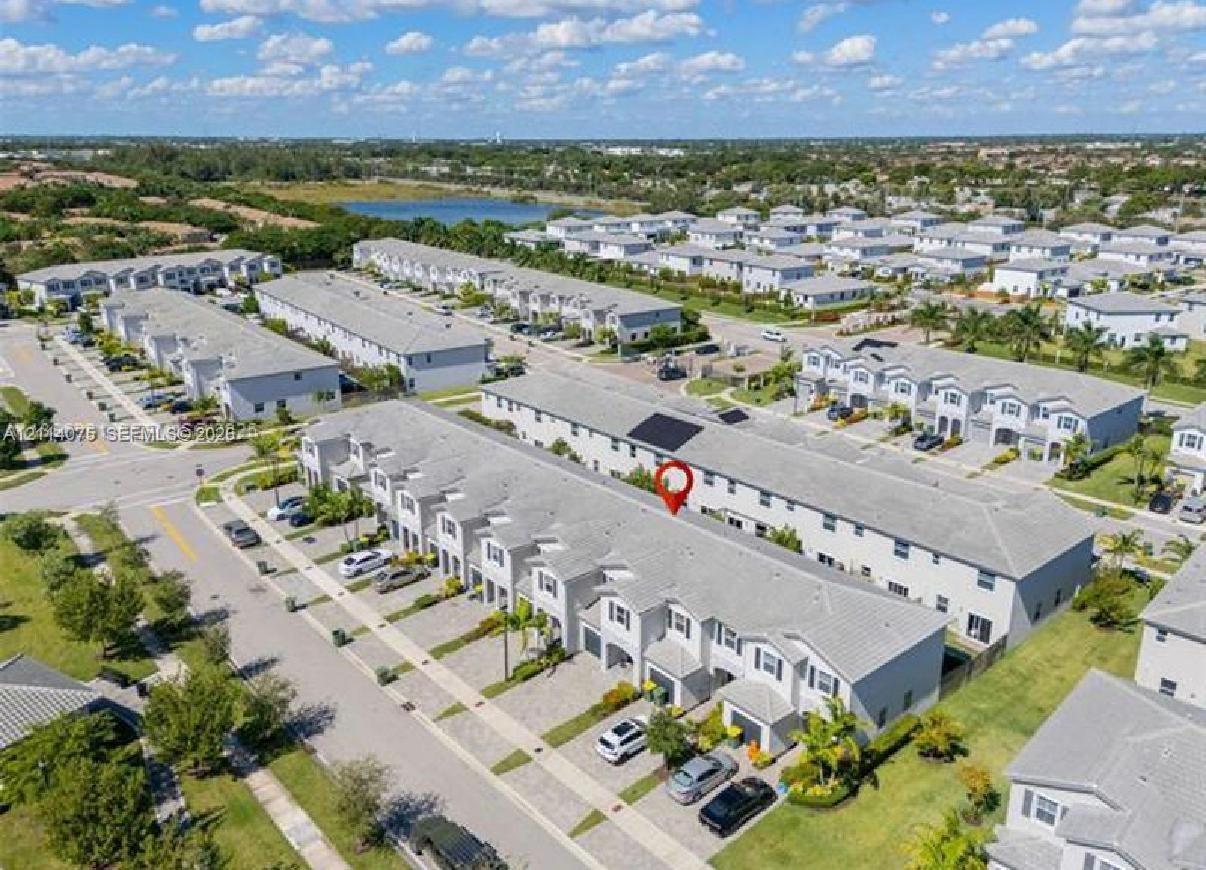 Aerial perspective of a multi-unit residential complex featuring gray shingle roofing, paved driveways, and surrounding green space