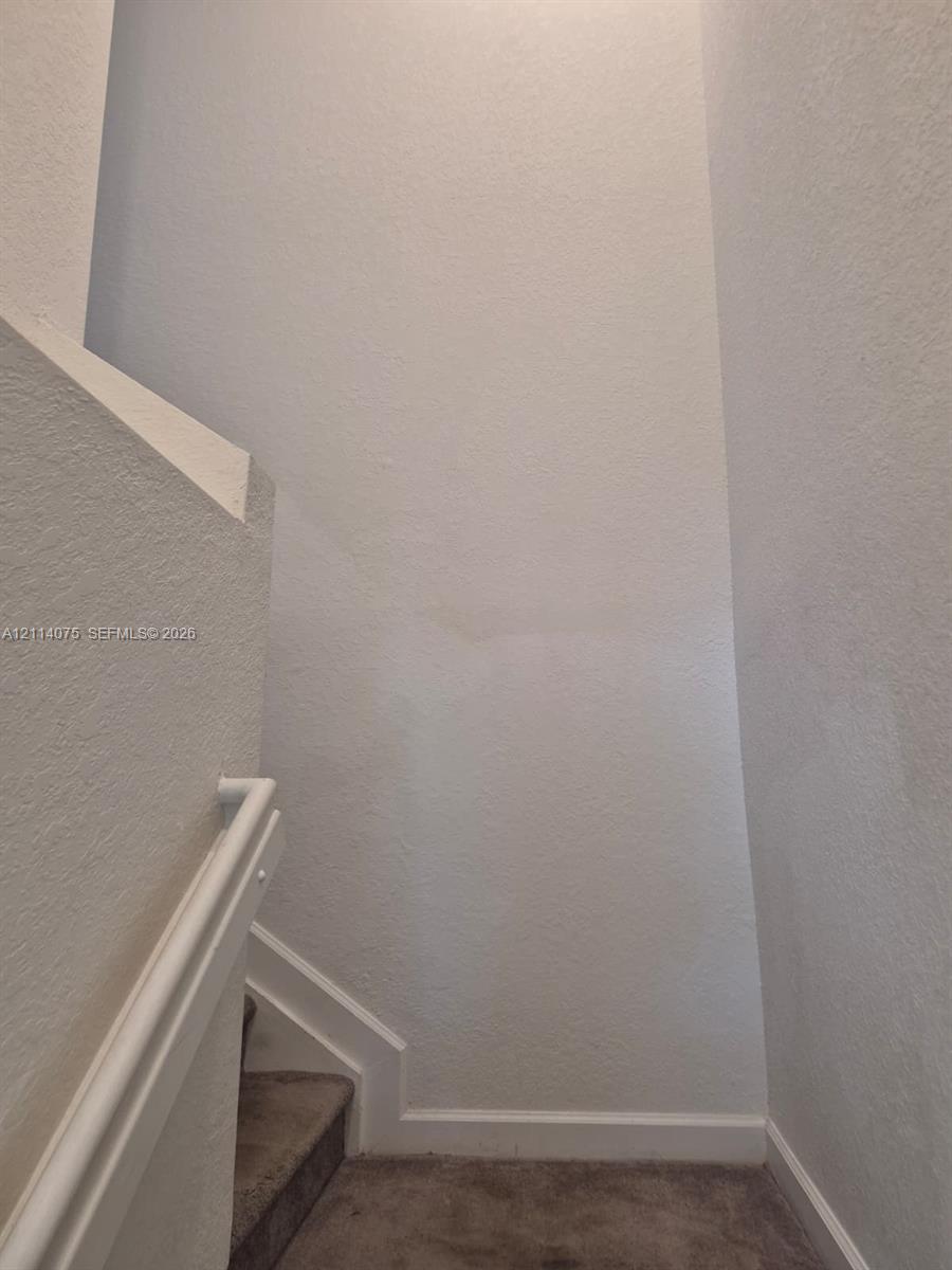 Staircase featuring neutral-toned carpeted treads and a painted white handrail