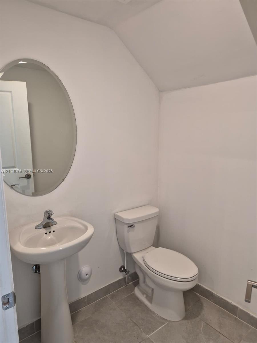 Oval wall-mounted mirror, white ceramic pedestal sink with chrome faucet, porcelain toilet, and neutral tile flooring