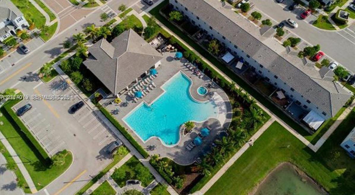 Community recreation center featuring an outdoor swimming pool, attached spa, paver deck, and surrounding palm trees
