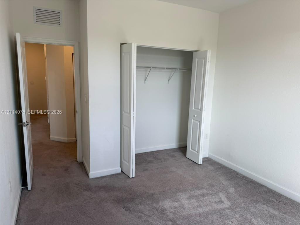 Interior room featuring neutral wall paint, carpeted flooring, and a closet with bifold doors and integrated shelving