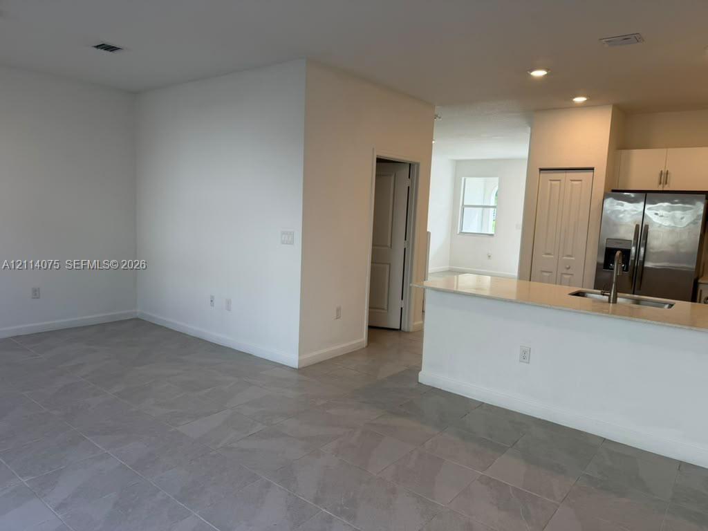 Open-concept area featuring stone-finish floor tile, recessed lighting, a kitchen island with a stone countertop, white cabinetry, and stainless steel appliances