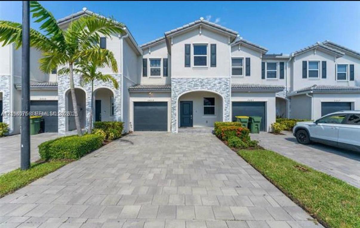 Two-story exterior featuring light stucco facade, decorative stone veneer detailing, arched entryways, private garages, and paved driveways Two-story exterior featuring light stucco facade, decorative stone veneer detailing, arched entryways, private garages, and paved driveways