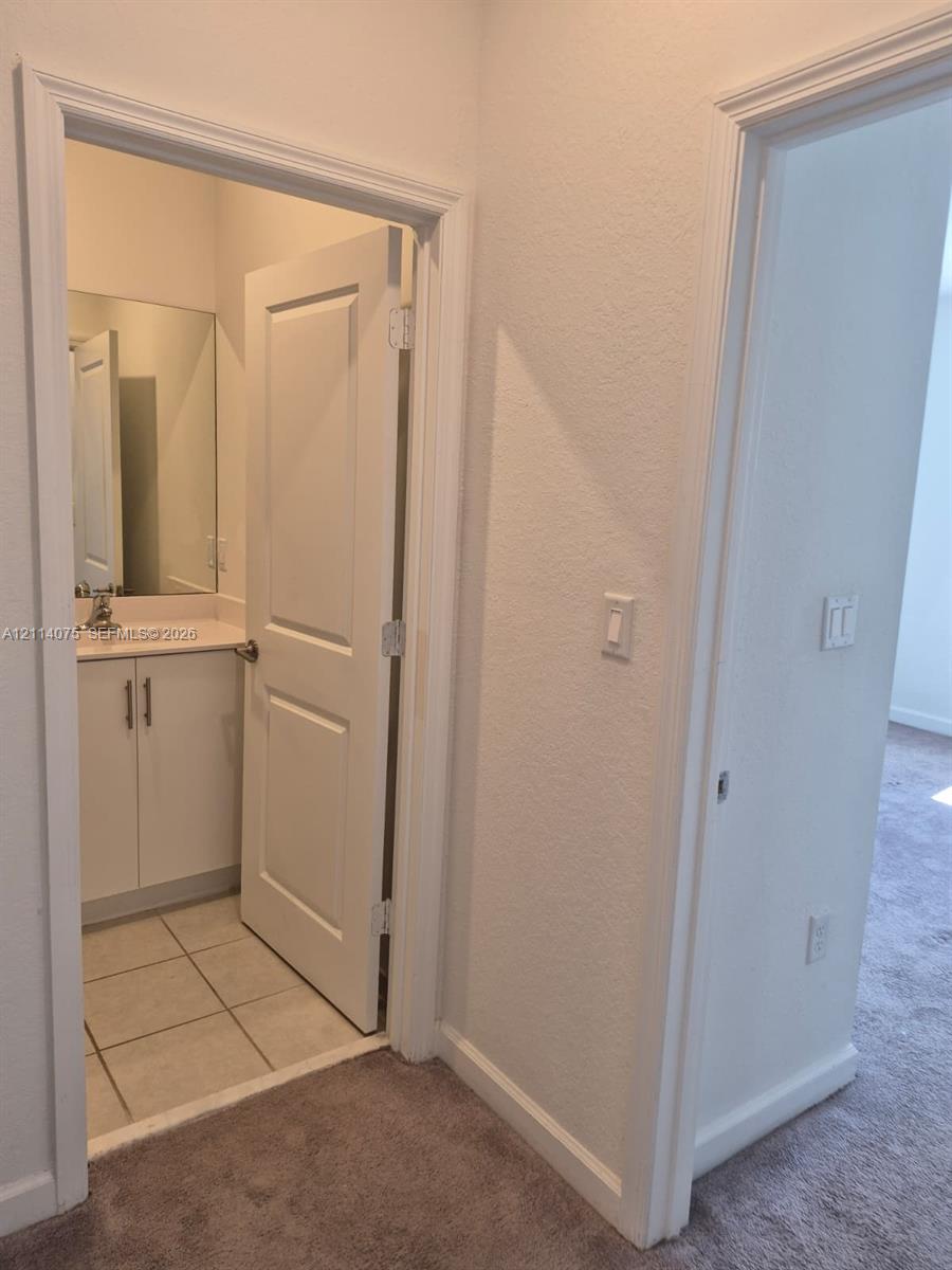 Bathroom featuring a white vanity cabinet with metallic hardware, integrated countertop with a sink, wall-mounted mirror, and tile flooring