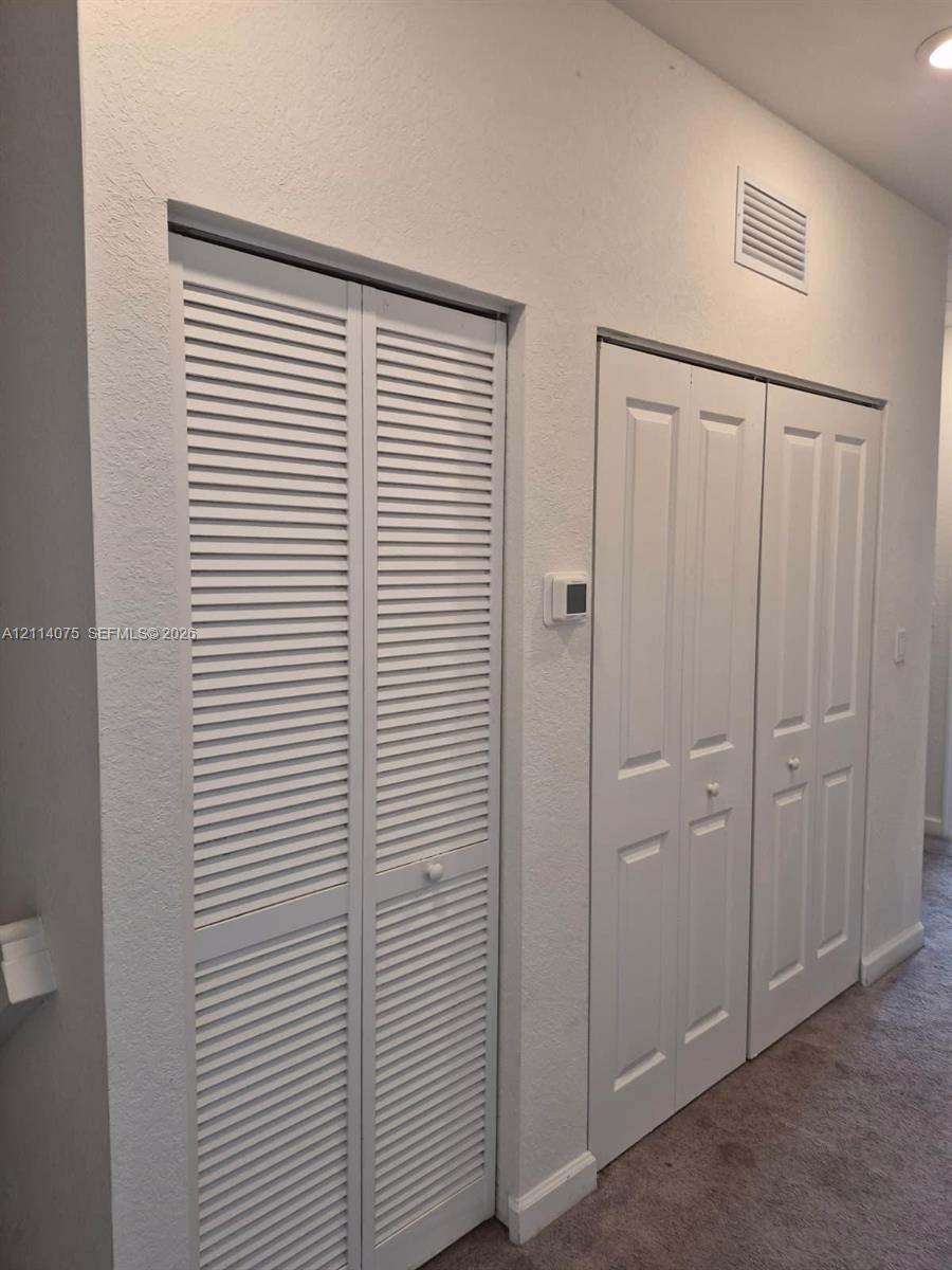 Wall-mounted thermostat featuring louvered bi-fold closet doors and dual-panel interior closet doors