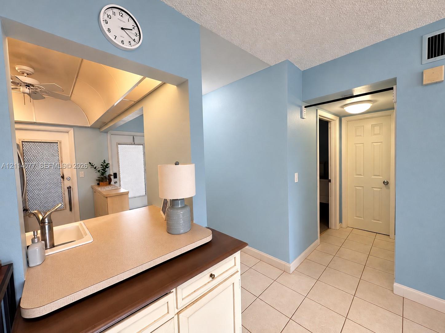 Kitchen passthrough featuring a solid-surface countertop and integrated sink with a chrome gooseneck faucet, accompanied by light-toned cabinetry and ceramic tile flooring
