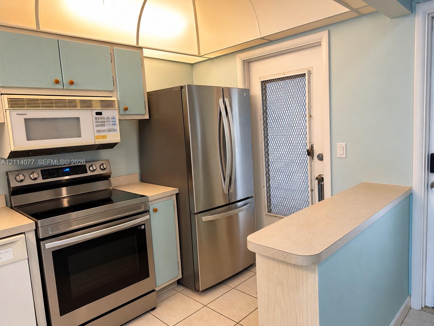 Kitchen featuring stainless steel refrigerator, over-the-range microwave, electric range, laminate countertops, and ceramic tile flooring