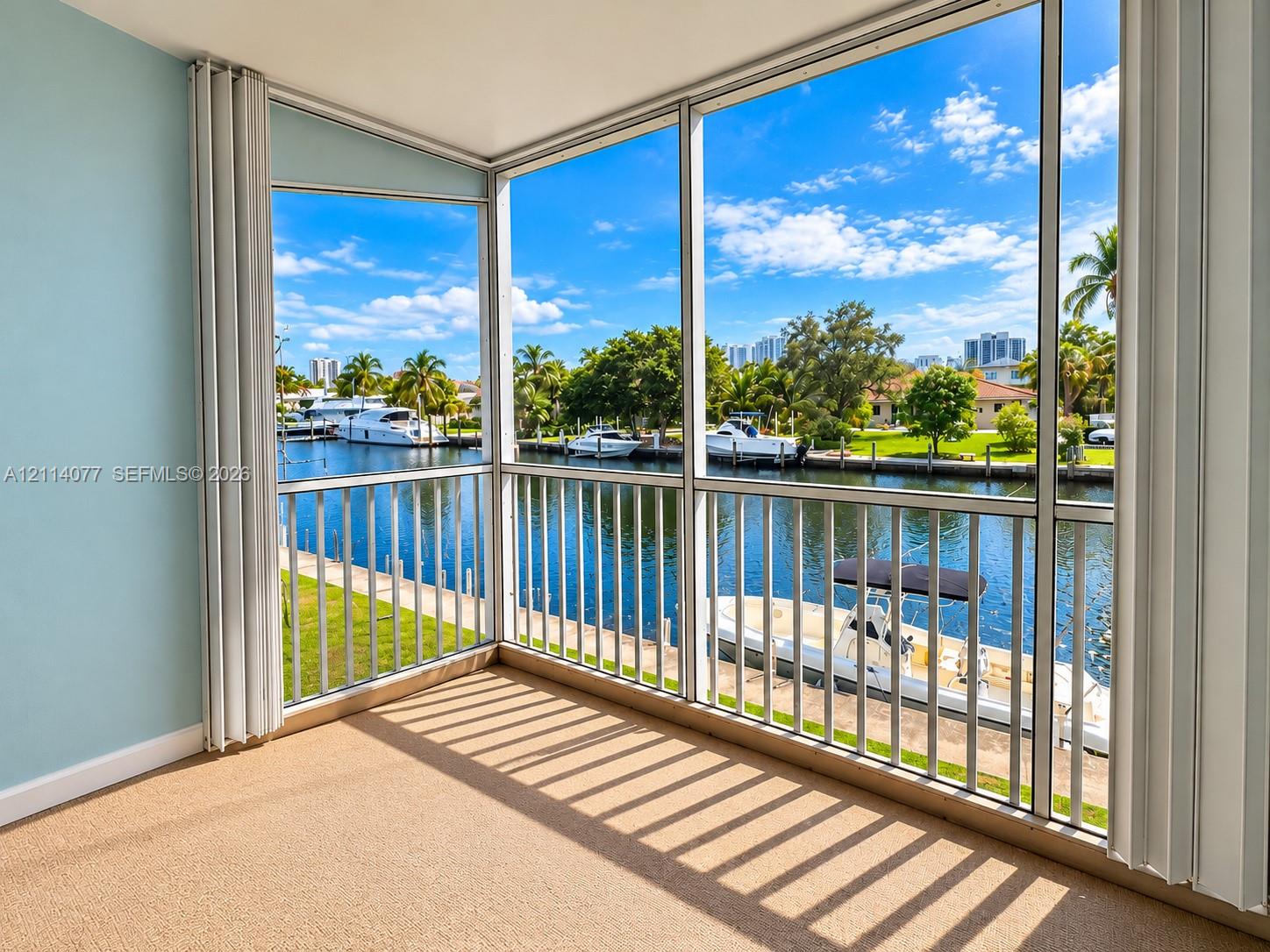 Enclosed balcony featuring floor-to-ceiling screened windows, white metal framing, and a bulkhead ceiling, overlooking a canal with maritime activity