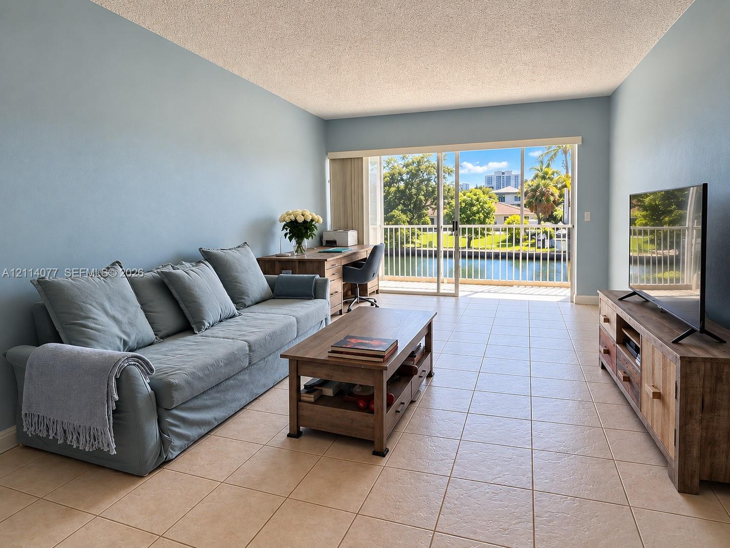 Living space featuring oversized sliding glass doors, neutral tile flooring, and a balcony with water frontage