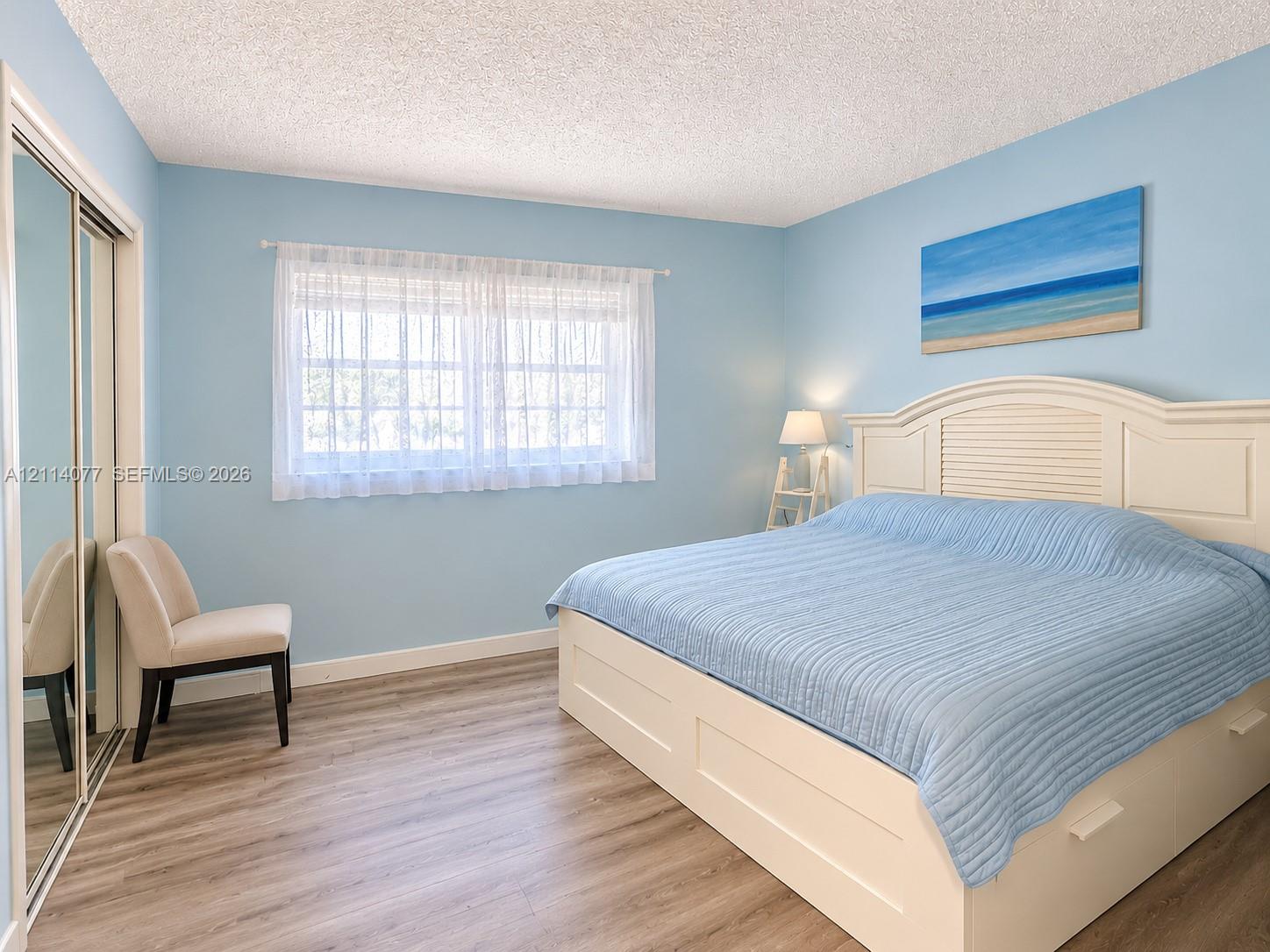 Room featuring wood-finish flooring, sliding mirrored closet doors, and a window with a sheer curtain treatment