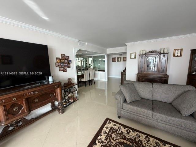 Living area featuring polished tile flooring, crown molding, and decorative architectural trim framing the doorway