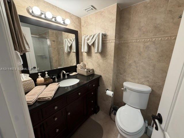 Dark-finish wooden cabinetry with integrated storage, dark stone-surfaced countertop, undermount sink, multi-bulb vanity lighting, and full-height wall tiling