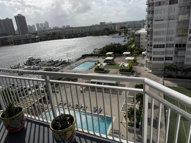 Elevated balcony with a white metal railing overlooking 2 swimming pool, tennis court, marina, and waterway