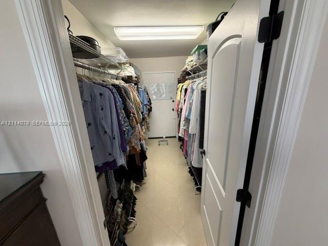 Walk-in closet featuring dual tiers of wire shelving, ceramic tile flooring, a solid-core interior door, and overhead flush-mount lighting