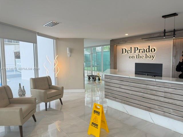 Lobby featuring polished tile flooring, floor-to-ceiling windows, and a reception desk with wood-slat detailing, stone countertop, and integrated backlighting