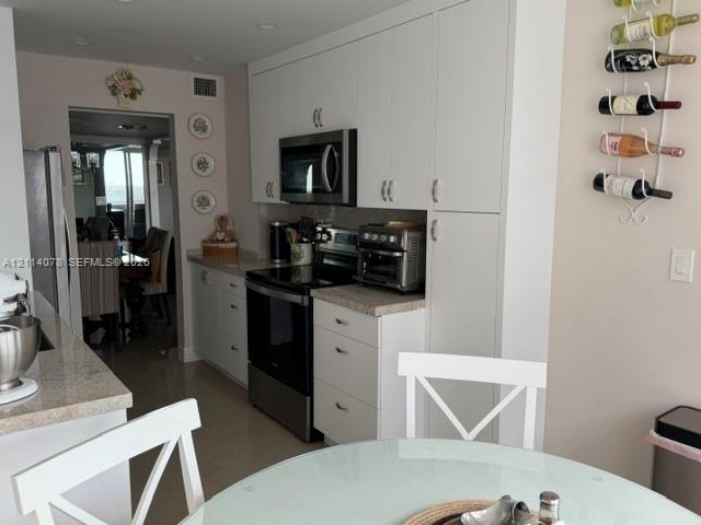 White cabinetry with integrated hardware, stainless steel appliances, neutral stone-finish countertops, and recessed lighting