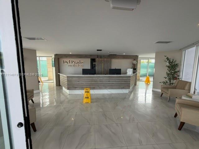 Reception area featuring large-format polished tile flooring, wood-paneled concierge desk with integrated lighting, and high-contrast signage