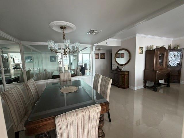 Dining area featuring large-format tile flooring, crown molding, a decorative ceiling medallion, an integrated wall mirror, and a multi-arm chandelier