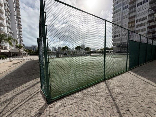 Tennis court featuring a green surface, chain-link perimeter fencing, and concrete paver decking