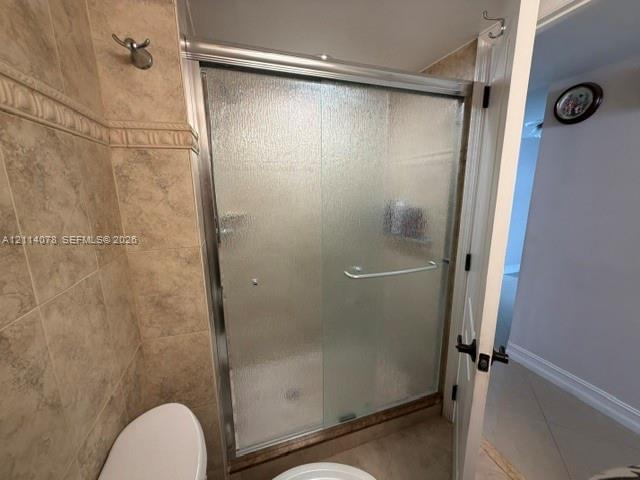 Shower enclosure with textured glass sliding doors, chrome framing, and coordinating metal hardware, featuring neutral-toned stone-finish wall tiling with decorative accent trim