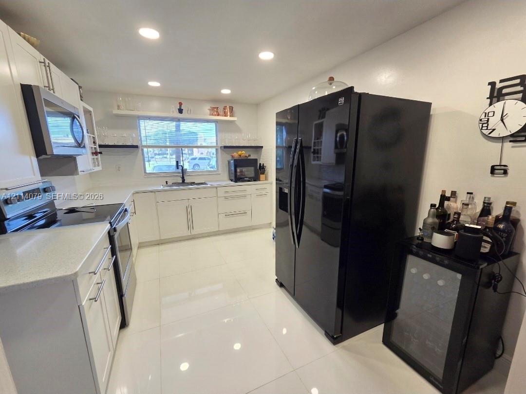 Kitchen featuring white cabinetry, solid-surface countertops, recessed ceiling lighting, light-toned tile flooring, and integrated black kitchen appliances Kitchen featuring white cabinetry, solid-surface countertops, recessed ceiling lighting, light-toned tile flooring, and integrated black kitchen appliances