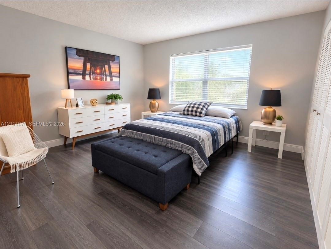 Bedroom featuring wood-finish flooring, a large window with horizontal blinds, and louvered double closet doors