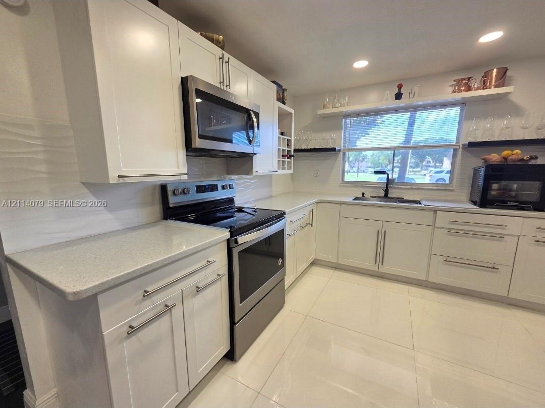 Kitchen featuring white cabinetry, solid-surface countertops, stainless steel appliances, a matte black faucet, and large-format tile flooring Kitchen featuring white cabinetry, solid-surface countertops, stainless steel appliances, a matte black faucet, and large-format tile flooring
