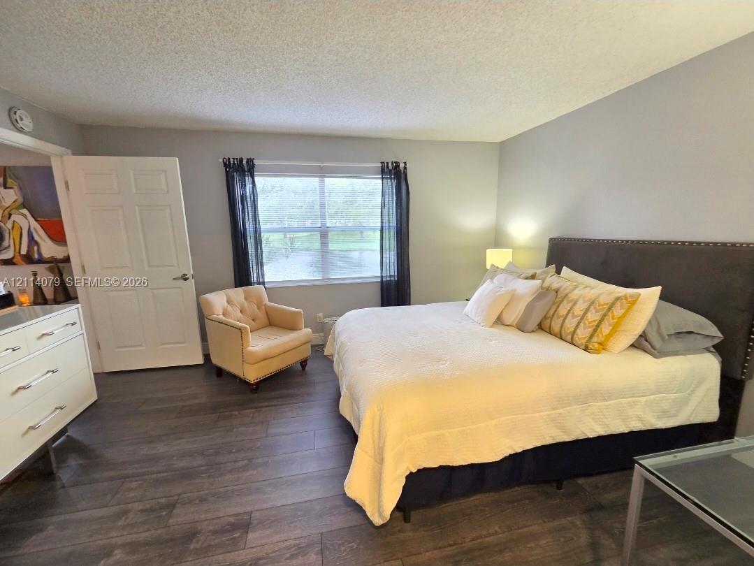 Room featuring wood-finish flooring, a large window, neutral wall paint, and a textured ceiling Room featuring wood-finish flooring, a large window, neutral wall paint, and a textured ceiling
