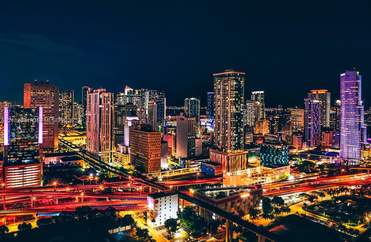 Aerial perspective of a high-density urban landscape featuring a skyline of illuminated skyscrapers and multi-level elevated infrastructure
