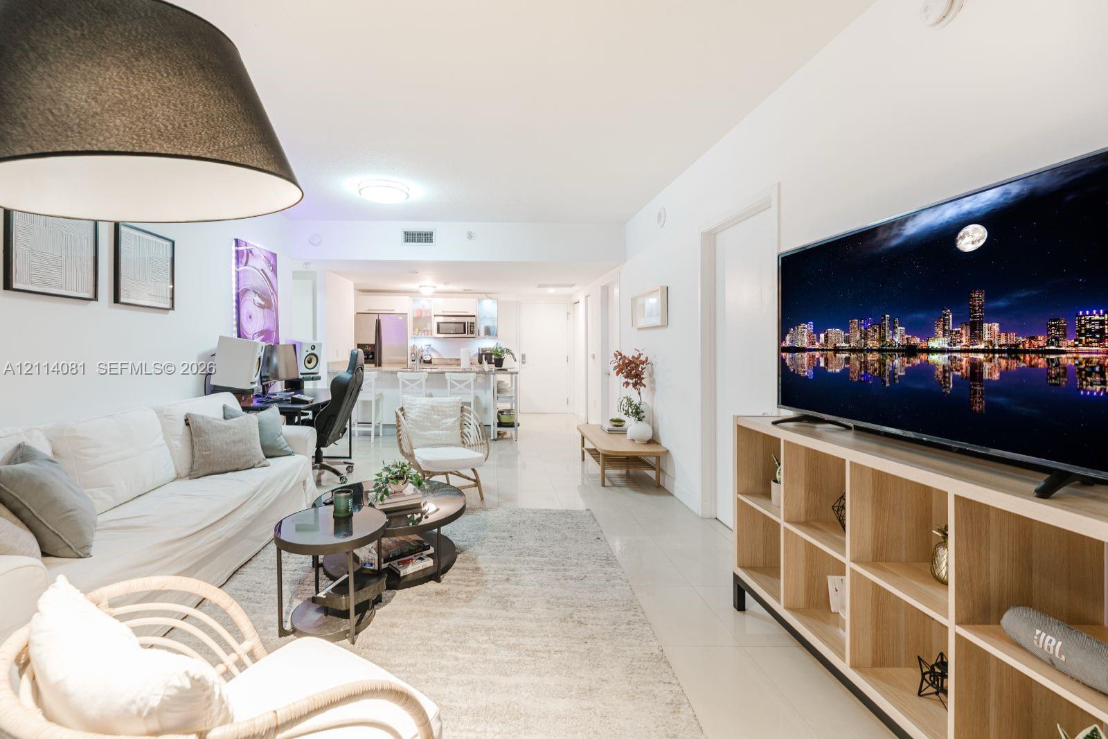 Open-concept interior featuring light-toned tile flooring, recessed lighting, and a kitchen equipped with a breakfast bar