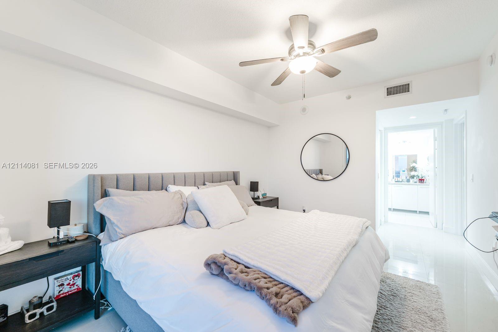 Neutral-toned room featuring high-gloss flooring, a ceiling fan with integrated lighting, and a circular wall-mounted mirror