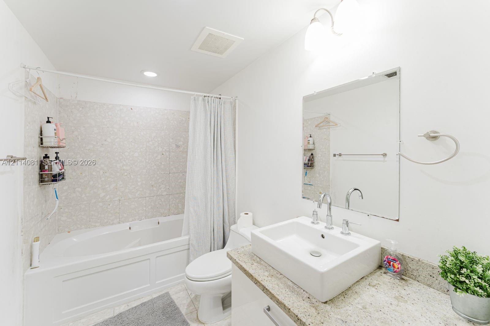 Bathroom featuring a vanity with an integrated vessel sink, stone-finish countertop, wall-mounted mirror, and a tub-shower combination with tile surround