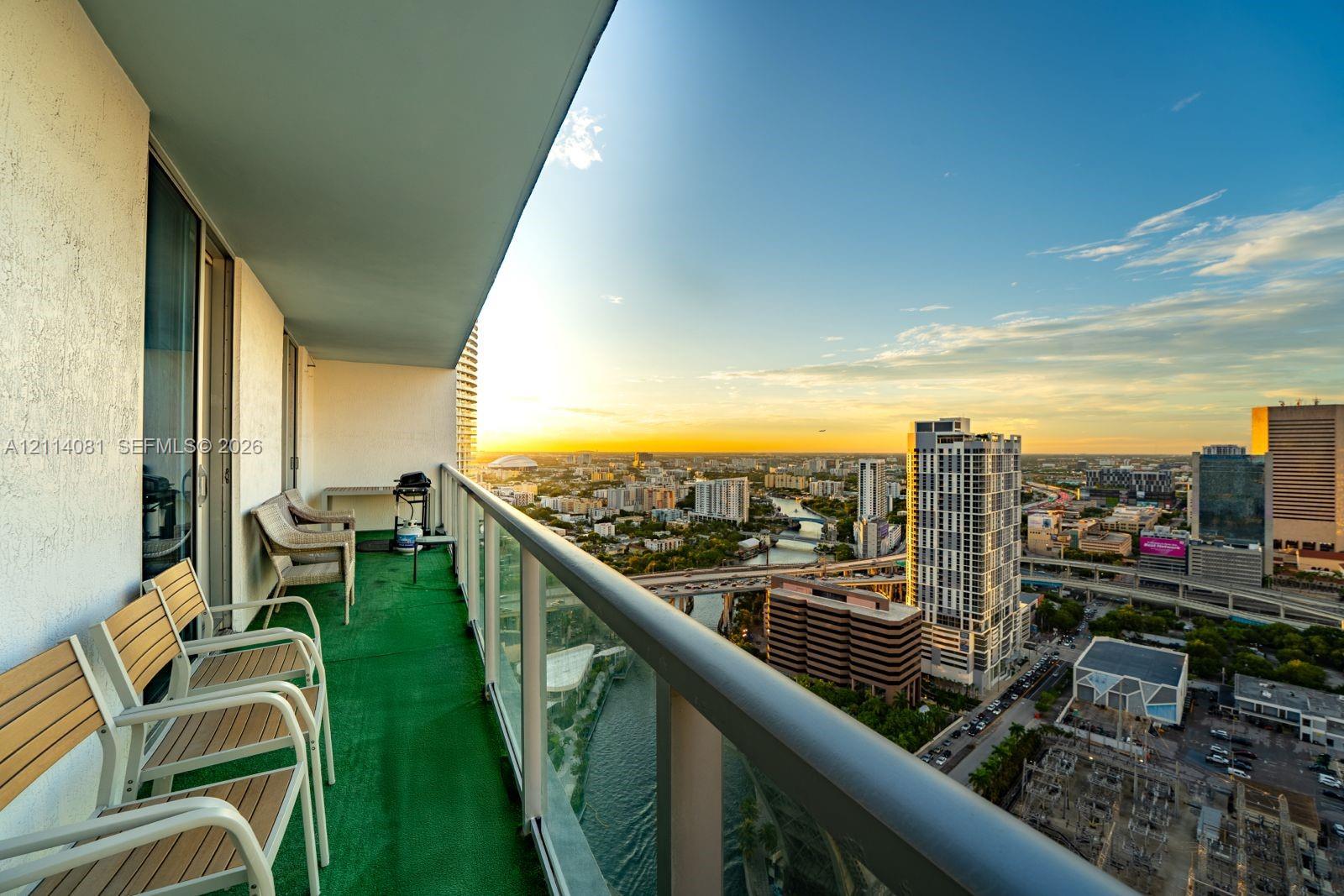 Covered balcony featuring metal railings with glass panels and a panoramic urban skyline backdrop