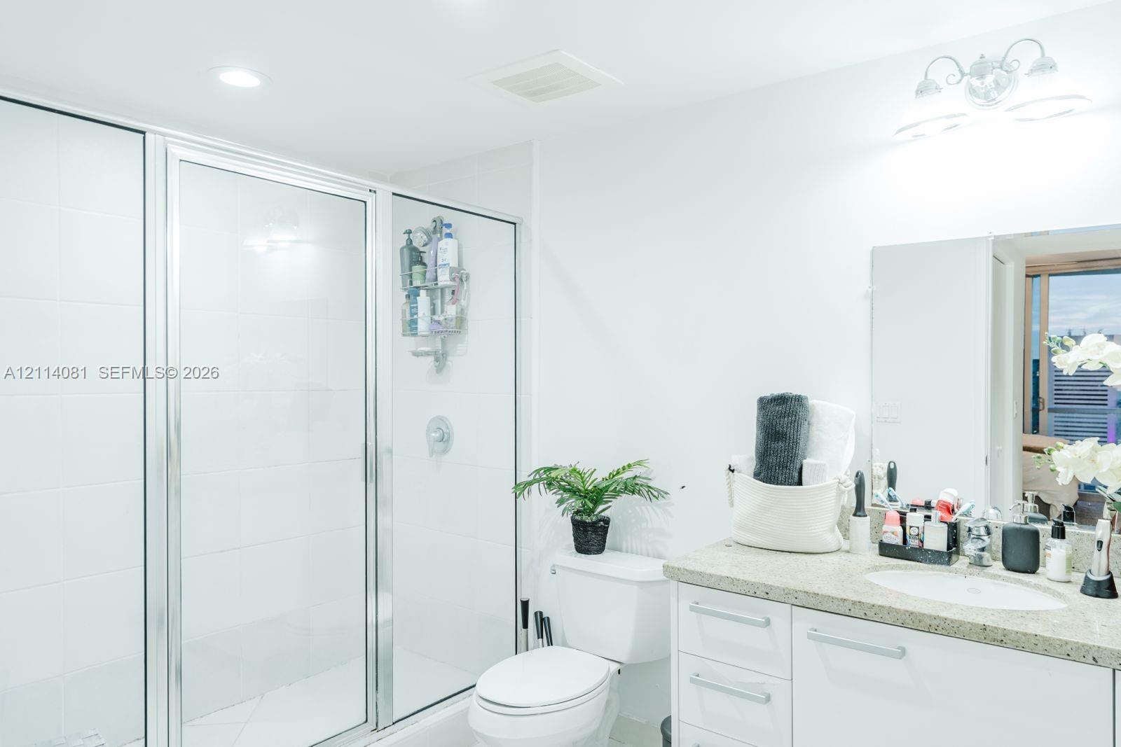 Bathroom featuring a glass-enclosed shower with white wall tile, a vanity with a stone-finish countertop and an integrated sink, and an attached multi-bulb light fixture