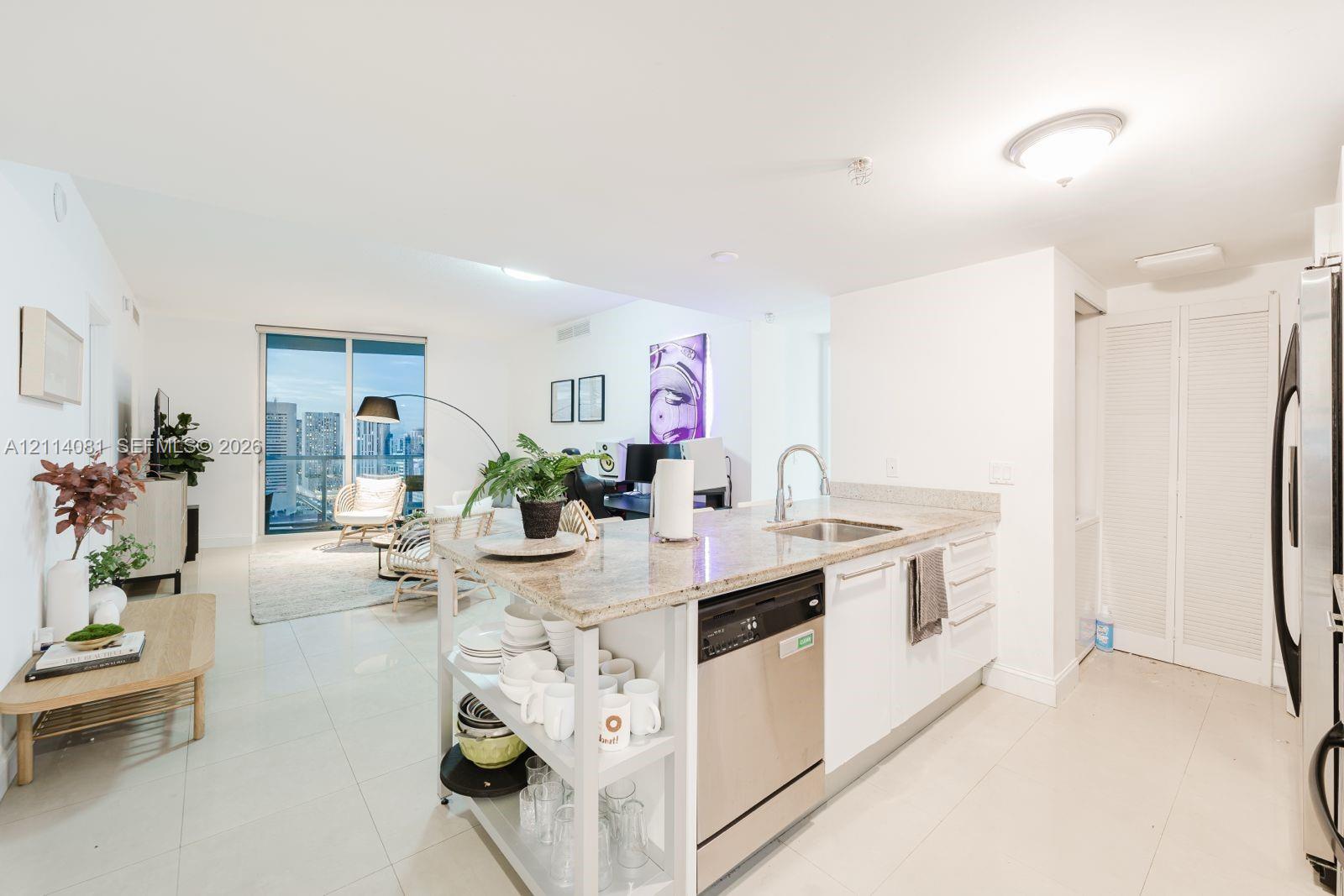 Kitchen featuring a stone-surface island, stainless steel dishwasher, integrated sink with a gooseneck faucet, white cabinetry, and light-tone tile flooring