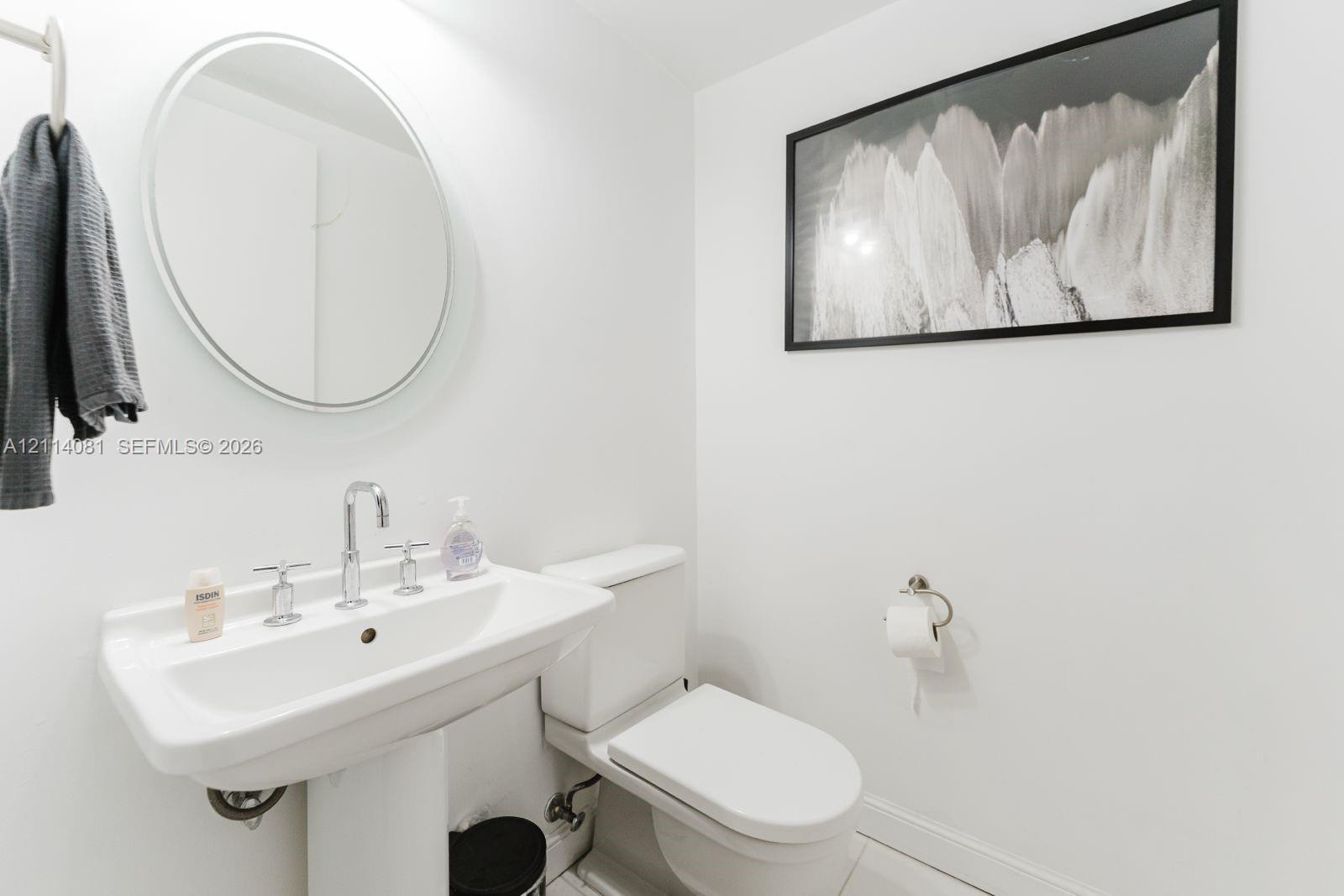 Pedestal sink with a widespread chrome faucet, oval wall-mounted mirror, and wall-mounted toilet paper holder