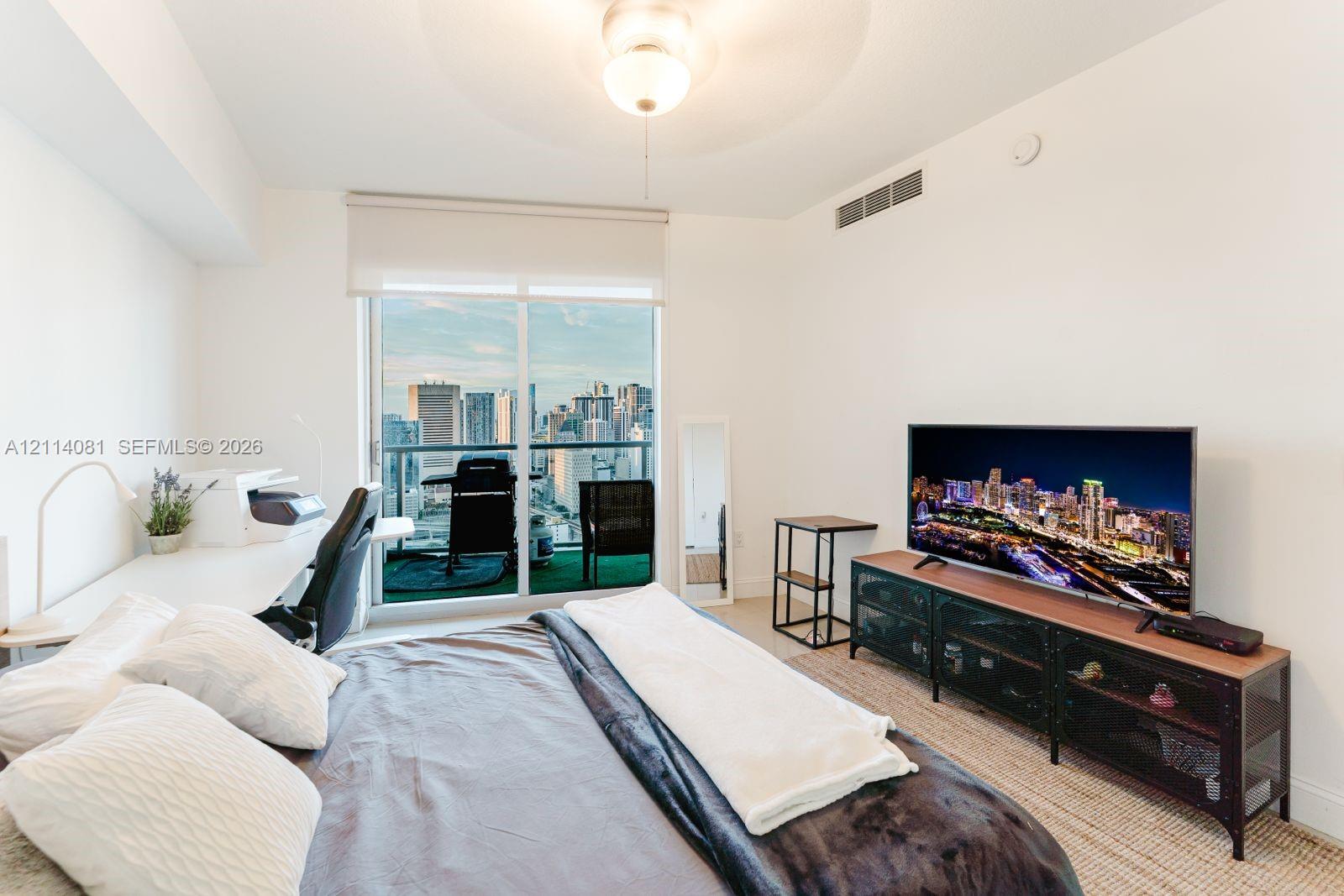 Floor-to-ceiling glass sliding door, private balcony, urban skyline backdrop, and central ceiling-mounted light fixture