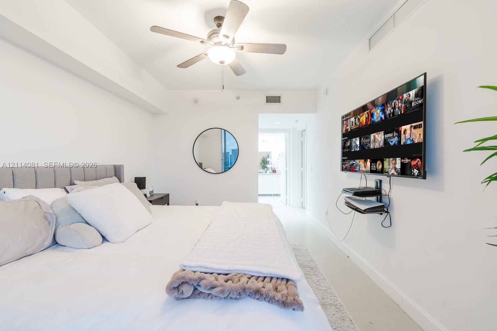 Neutral interior space featuring white walls, a ceiling-mounted light fixture with integrated fan, and a circular wall-mounted mirror