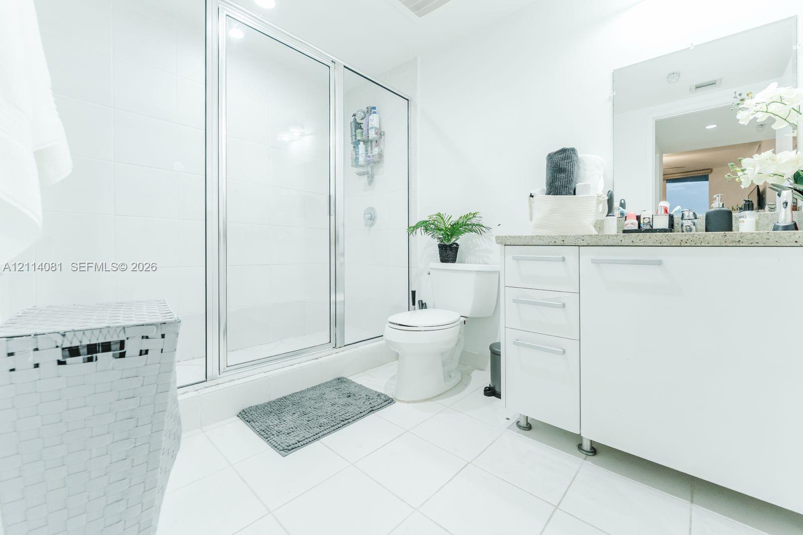 Bathroom featuring a white vanity with integrated cabinetry, a solid surface countertop, a wall-mounted mirror, and a walk-in shower enclosure with a glass door
