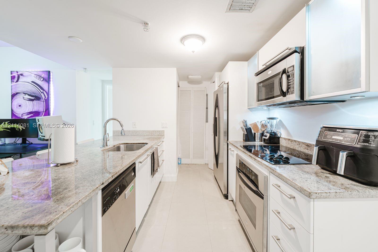 Kitchen featuring stone countertops, white cabinetry, integrated stainless steel appliances, and tile flooring