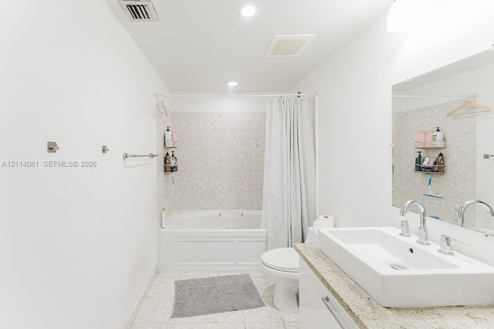 Bathroom featuring a soaking tub with decorative tile surround, a rectangular vessel sink, stone-finish countertop, and recessed lighting