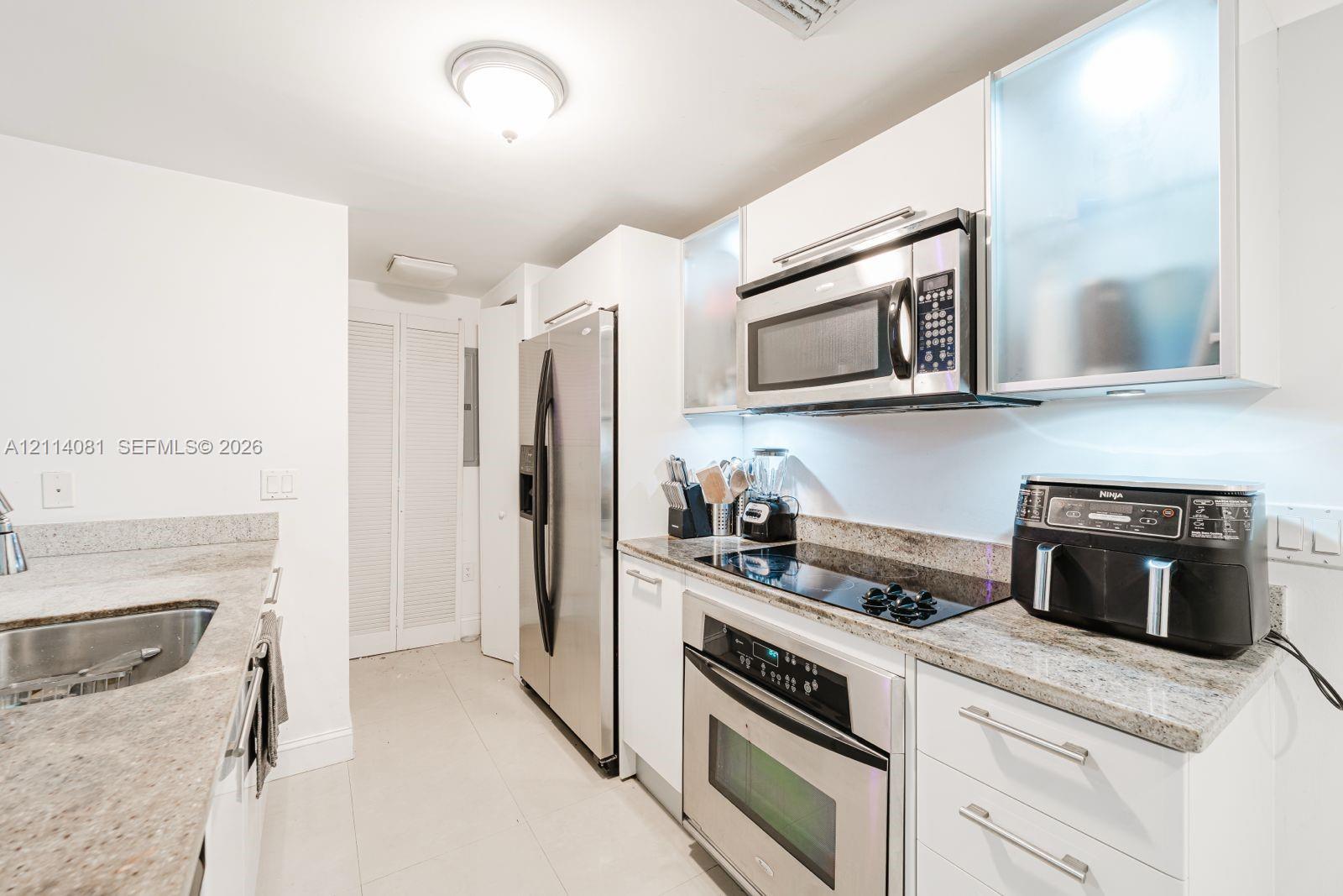 Kitchen featuring white cabinetry with frosted glass upper panels, stone countertops, stainless steel appliances, and integrated lighting