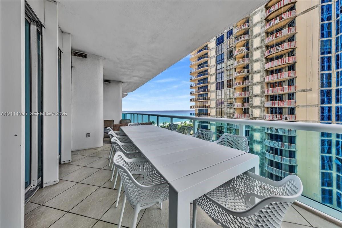 Covered balcony featuring oversized neutral floor tiles and a glass-paneled railing overlooking the ocean
