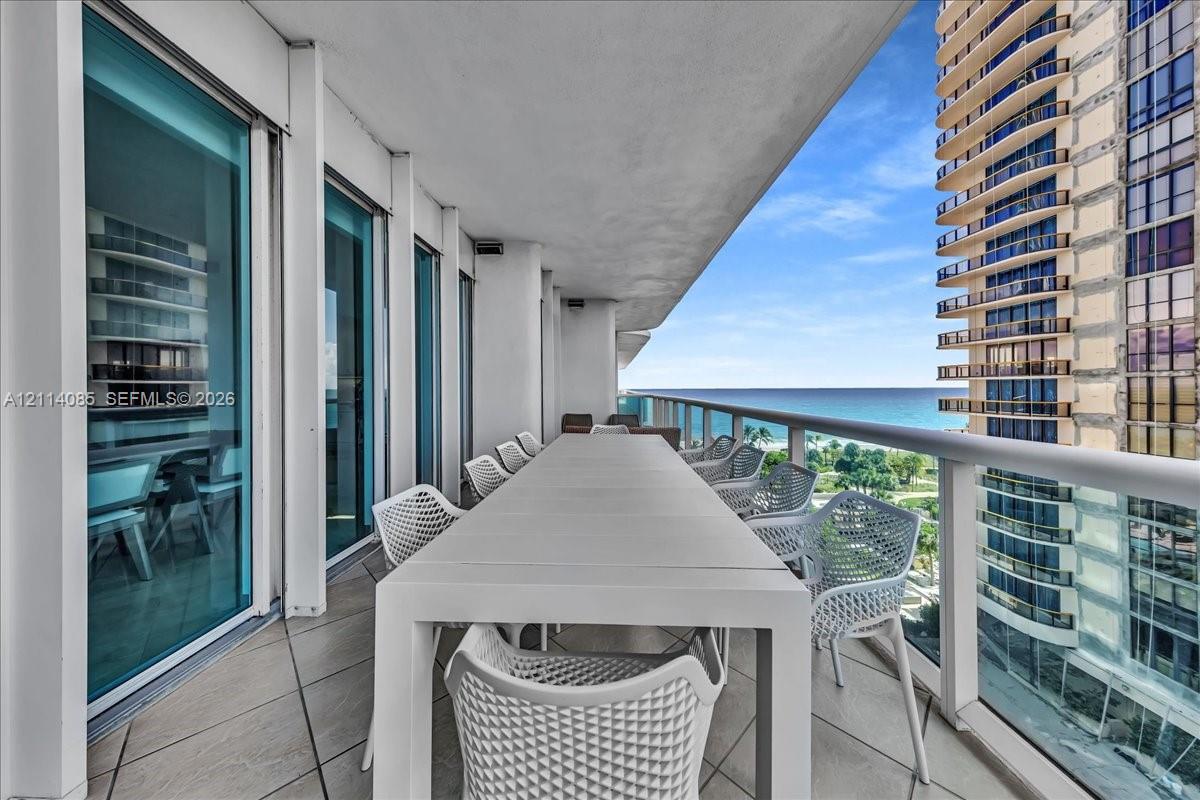Spacious covered balcony featuring large-format tile flooring, floor-to-ceiling glass panels, and a metal railing