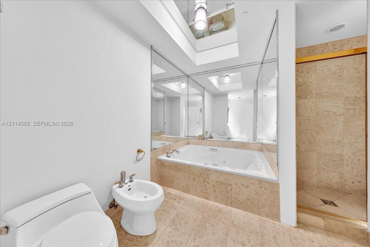 Jetted soaking tub with tile surround, walk-in shower with tile walls, bidet, and floor-to-ceiling mirrored walls featuring a skylight