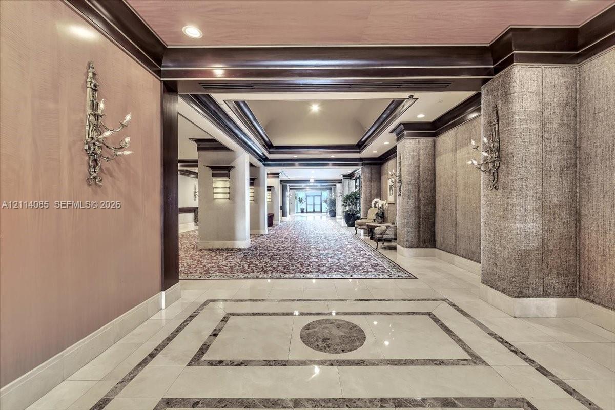 Grand entrance featuring polished stone flooring with geometric inlays, wood-paneled walls, heavy crown molding, recessed lighting, and ornate wall-mounted sconces