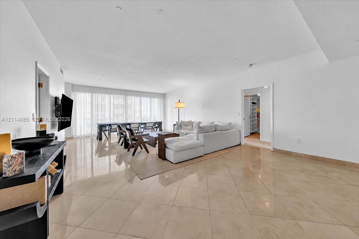 Open-concept living space featuring high ceilings, polished stone-finish tile flooring, and floor-to-ceiling windows with integrated drapery tracks