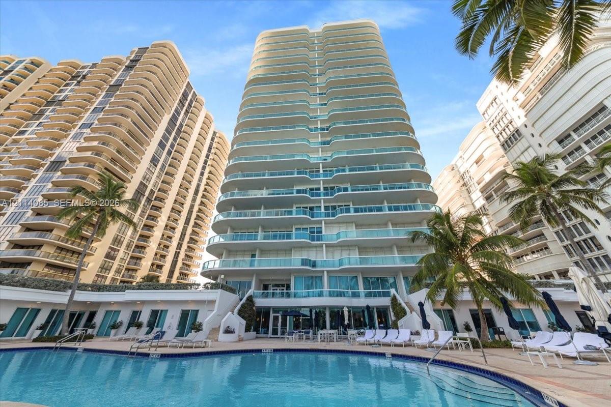 High-rise exterior featuring glass-railed private balconies, a multi-level concrete facade, and a ground-level swimming pool with paved decking and mature palm trees